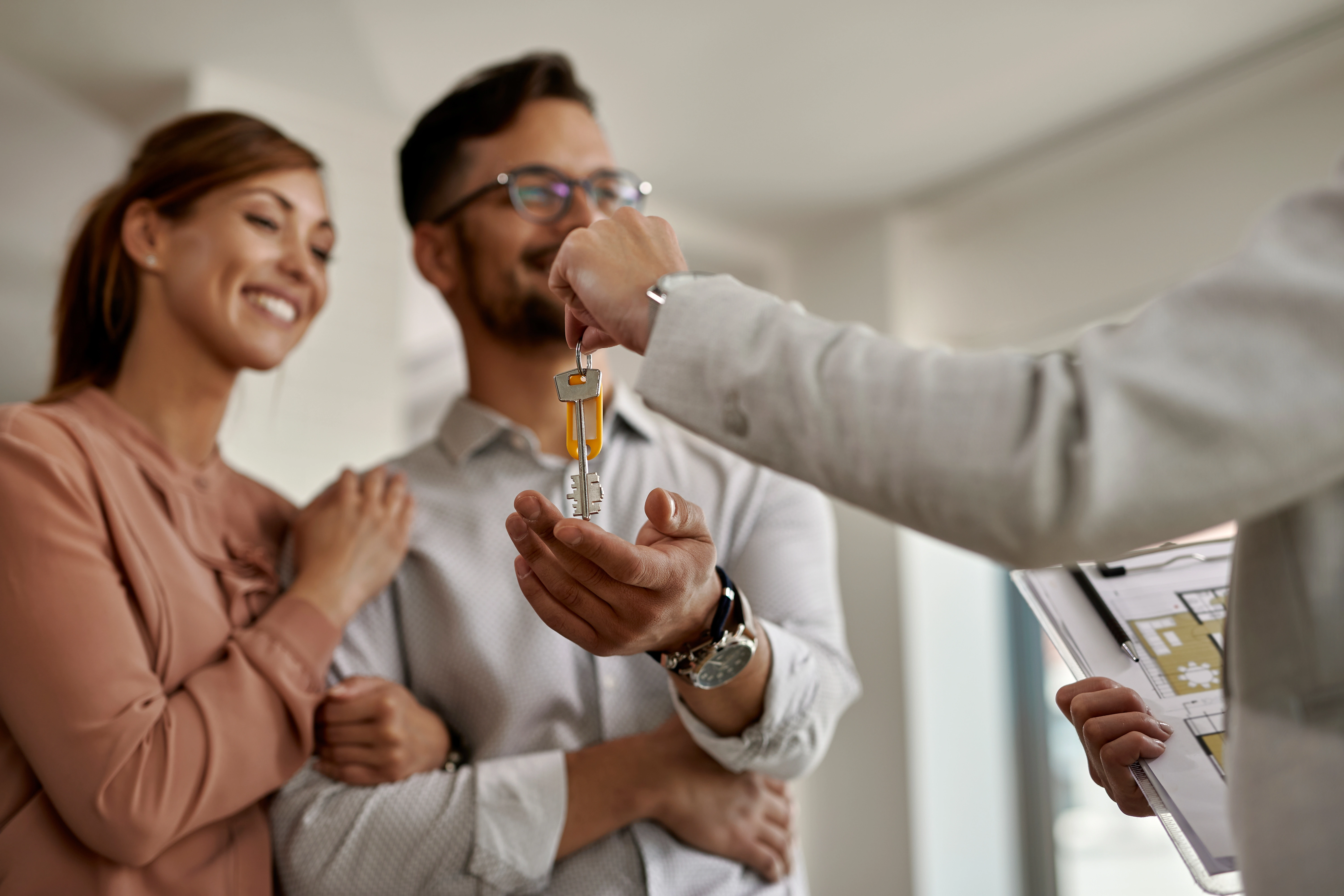 A real estate agent San Clemente CA hands house keys to a couple purchasing their new home.