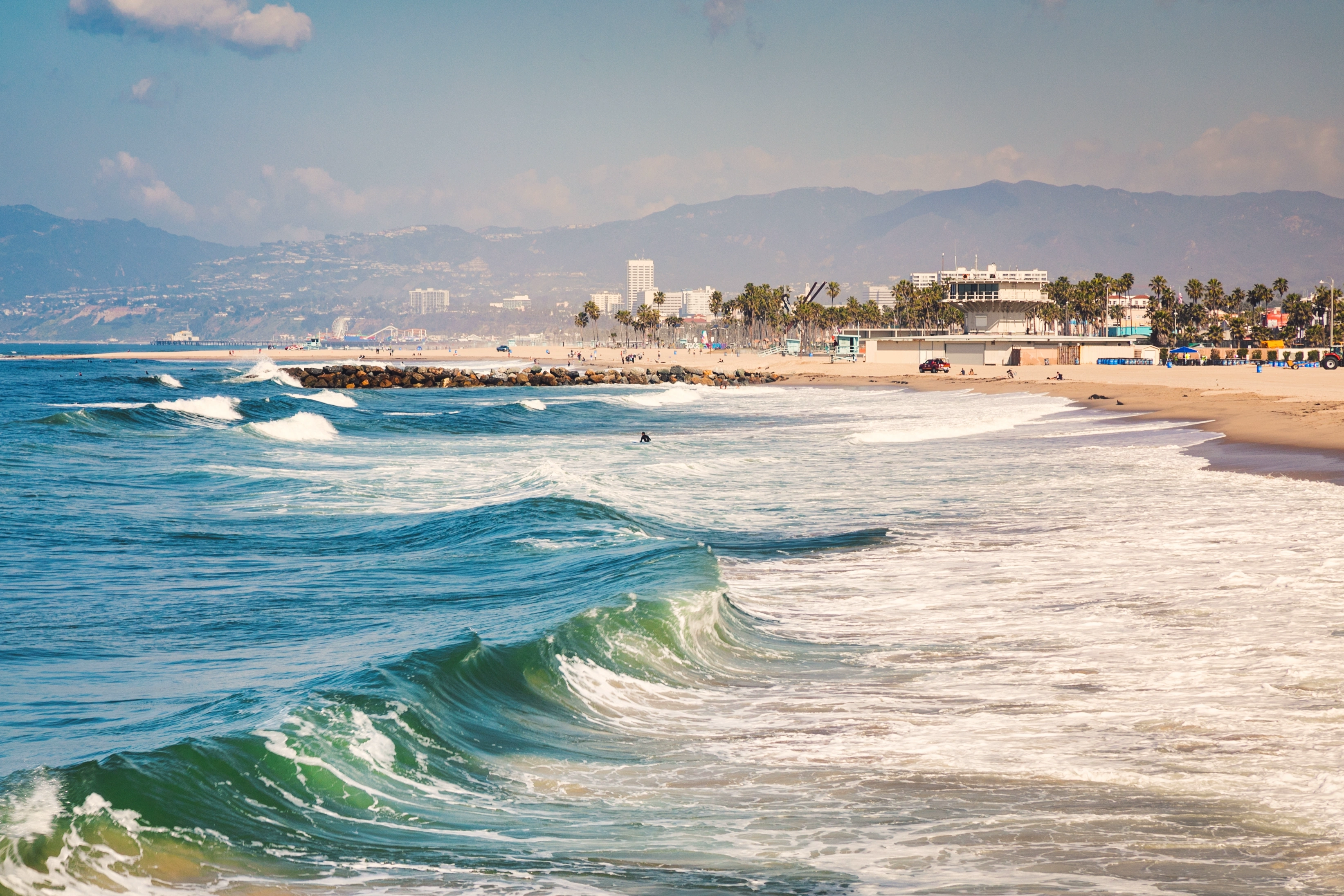 Rolling ocean waves along a sandy beach with a distant coastal city and mountains, ideal for buying a home in San Clemente.