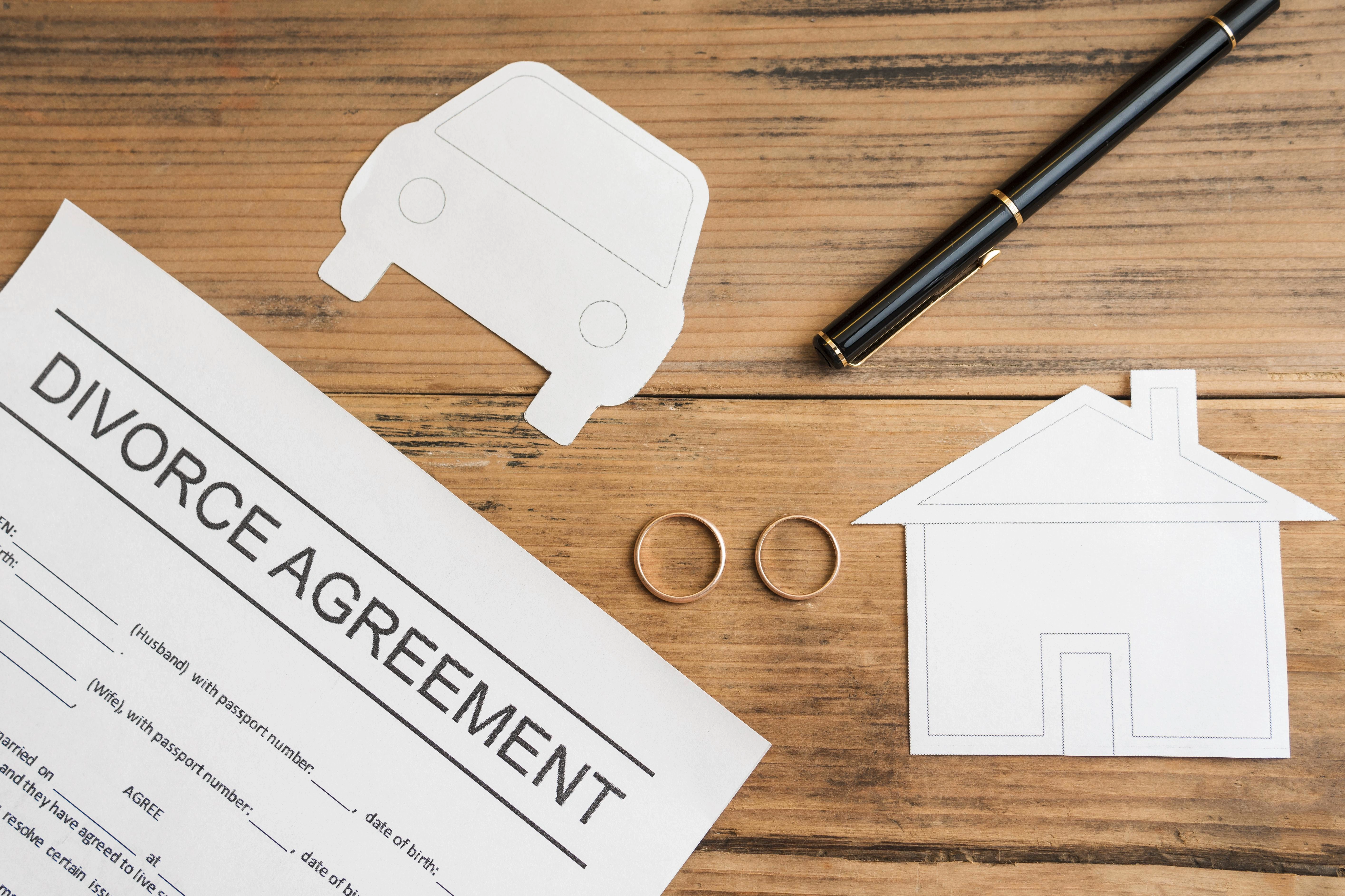 Divorce agreement paperwork next to a paper house cutout, representing selling home during divorce Orange County.
